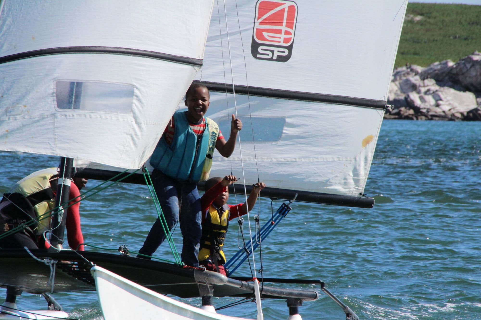 Young sailors in life jackets standing on a Hobie trampoline with an instructor